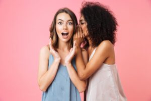 two female friends, sharing a secret. pink background