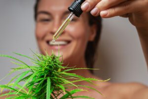 fresh faced woman, dropping CBD oil on a hemp flower