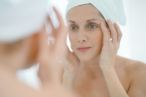 woman in a towel headwrap, looking in a mirror, at fine lines and wrinkles