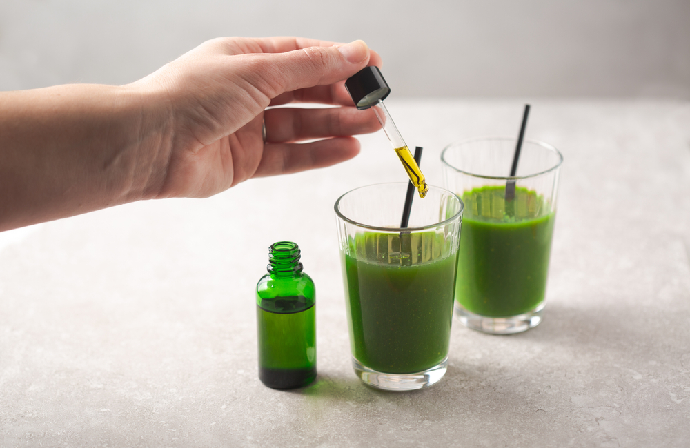 a hand putting a dose of CBD into green juice.