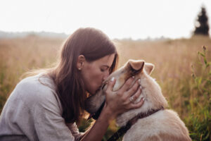 woman kissing dog on head, in field